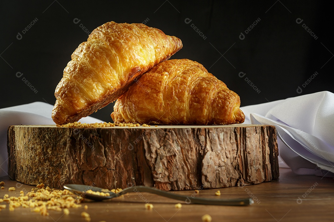 Deliciosos croissants em tronco de madeira, com toalha branca ao redor.