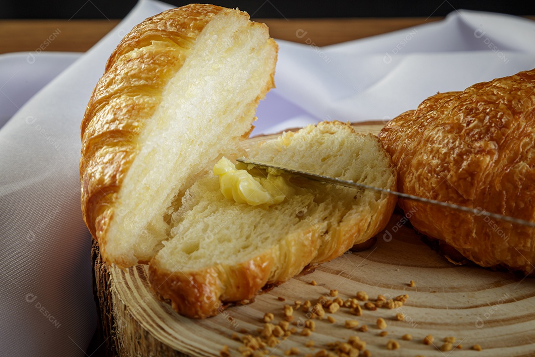 Deliciosos croissants em tronco de madeira, com toalha branca ao redor.