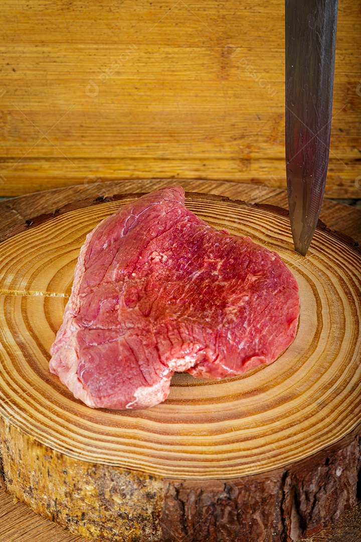 Bife de picanha cru em fundo de madeira em estilo rústico.