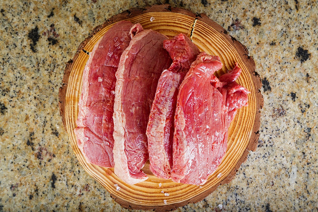 Bife de picanha cru em fundo de madeira em estilo rústico.