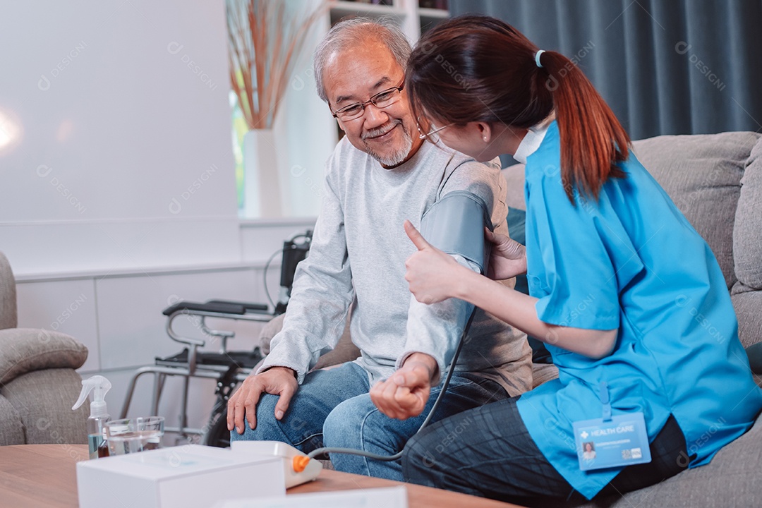 O médico cuidador asiático examina o medidor de pressão arterial de uso de paciente mais velho.
