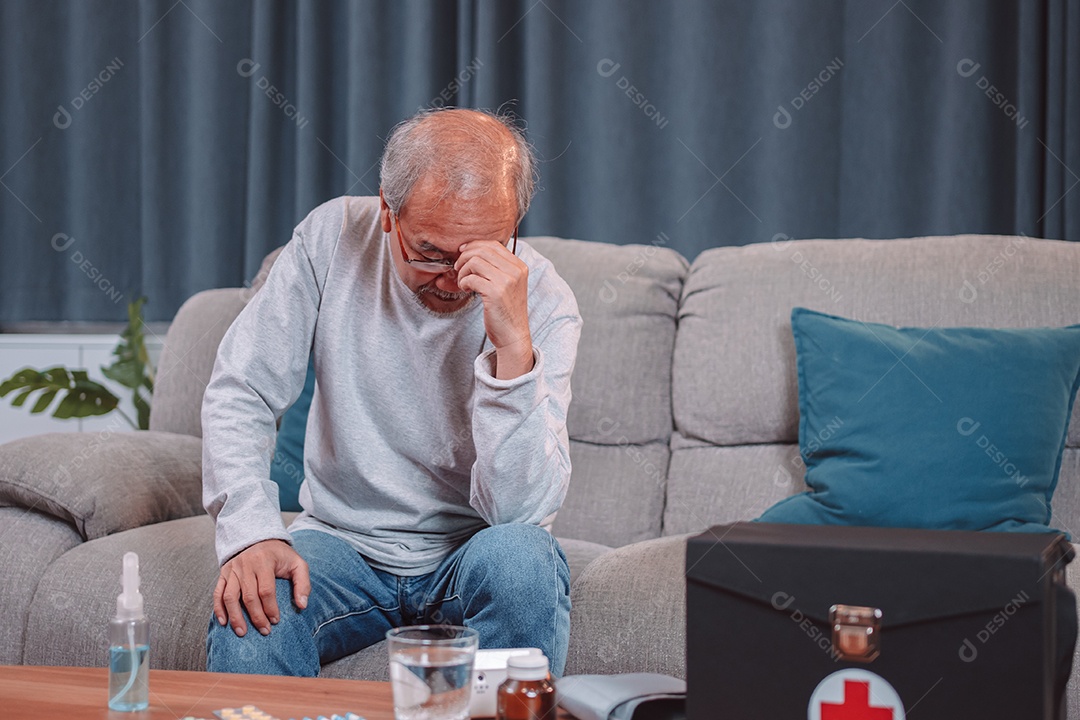 Idoso maduro asiático sente dor de cabeça por estresse sentado no sofá na sala de estar.