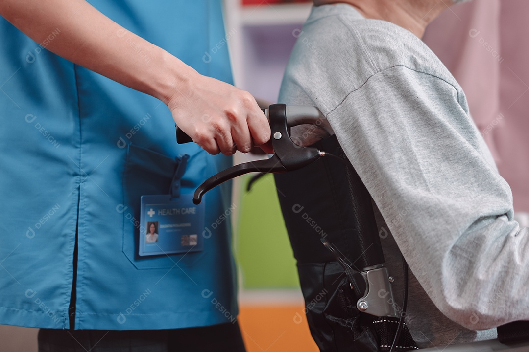 Enfermeira cuidadora asiática apoia idoso sênior em cadeira de rodas na sala de estar.