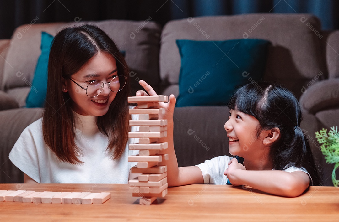 A família feliz asiática da filha joga bloco de madeira de brinquedo em casa.
