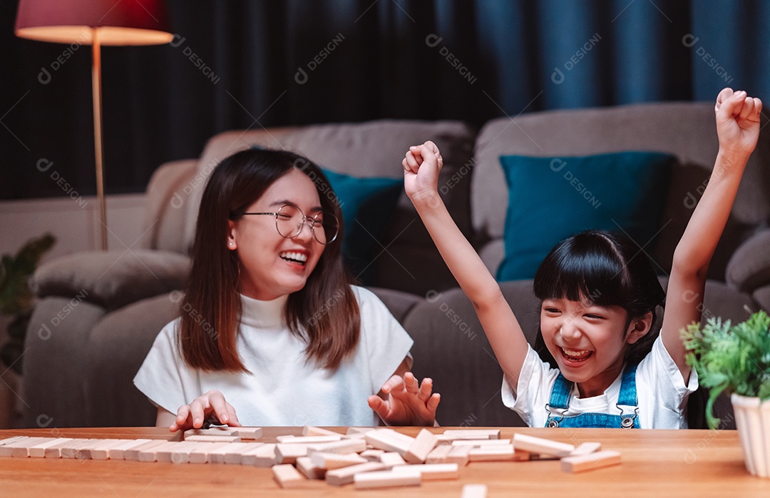 A família feliz asiática da filha joga bloco de madeira de brinquedo em casa.