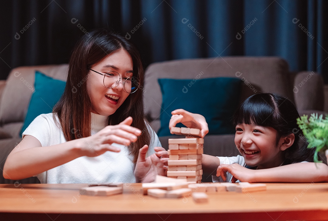 A família feliz asiática da filha joga bloco de madeira de brinquedo em casa.