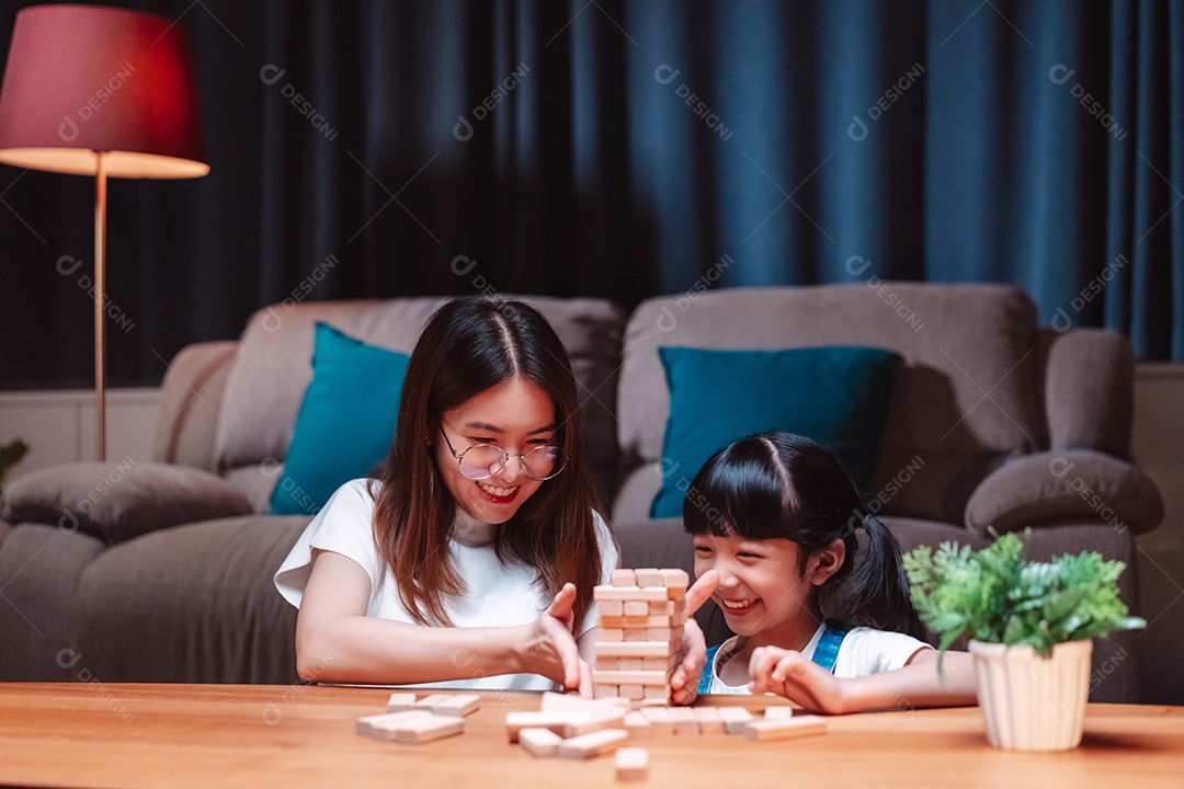 A família feliz asiática da filha joga bloco de madeira de brinquedo em casa.