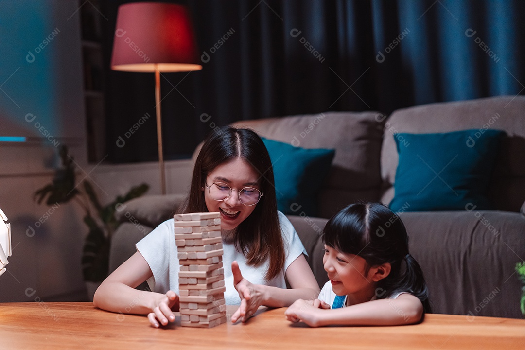 A família feliz asiática da filha joga bloco de madeira de brinquedo em casa.