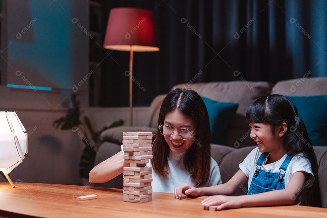 A família feliz asiática da filha joga bloco de madeira de brinquedo em casa.