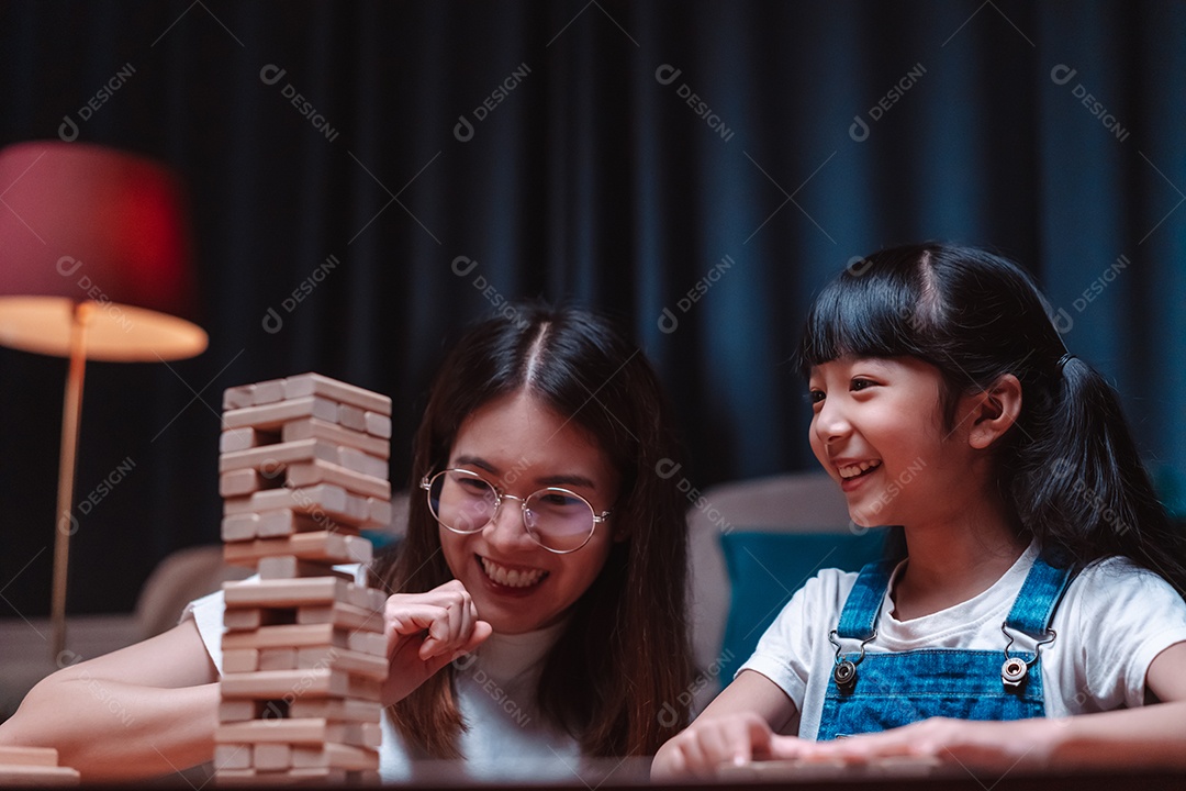 A família feliz asiática da filha joga bloco de madeira de brinquedo em casa.