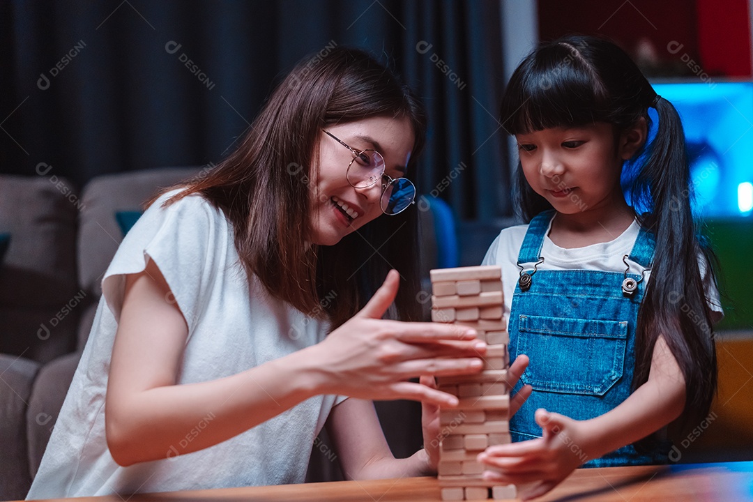 A família feliz asiática da filha joga bloco de madeira de brinquedo em casa.