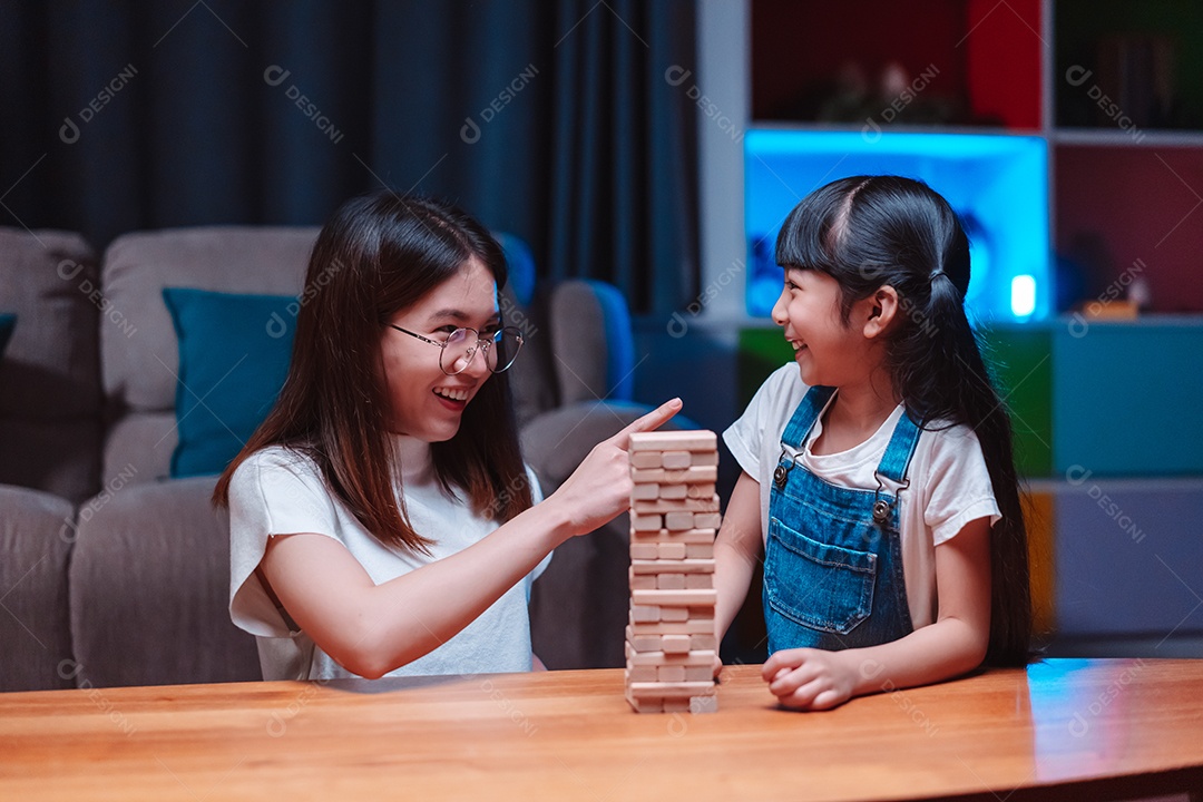 A família feliz asiática da filha joga bloco de madeira de brinquedo em casa.