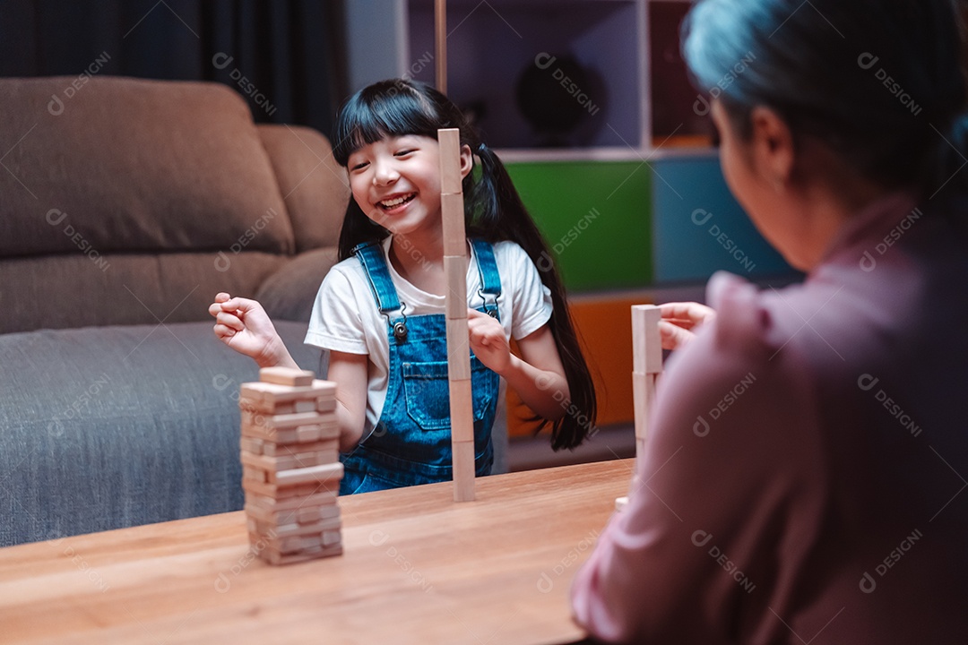 A família feliz asiática da filha joga bloco de madeira de brinquedo em casa.