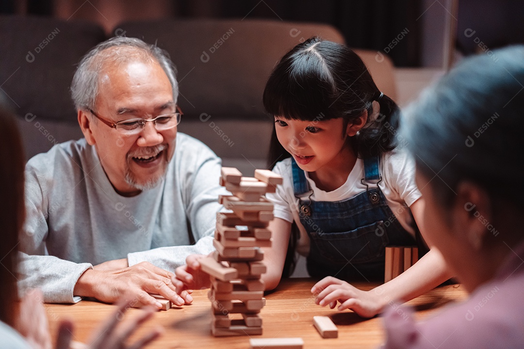 A família feliz asiática da filha joga bloco de madeira de brinquedo em casa.