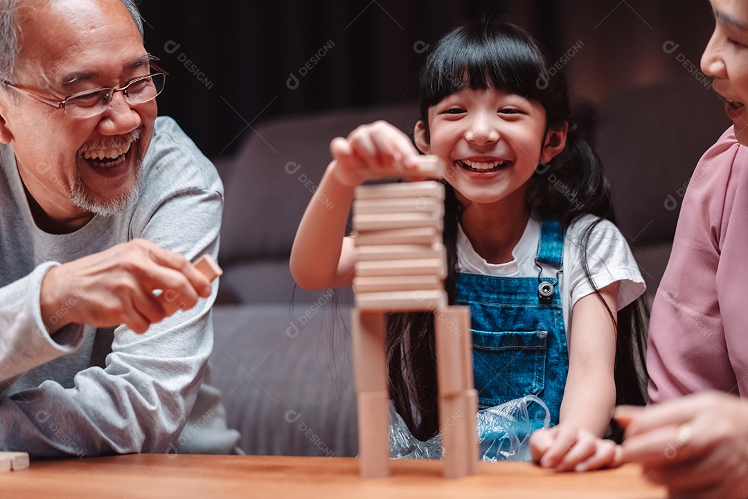 A família feliz asiática da filha joga bloco de madeira de brinquedo em casa.