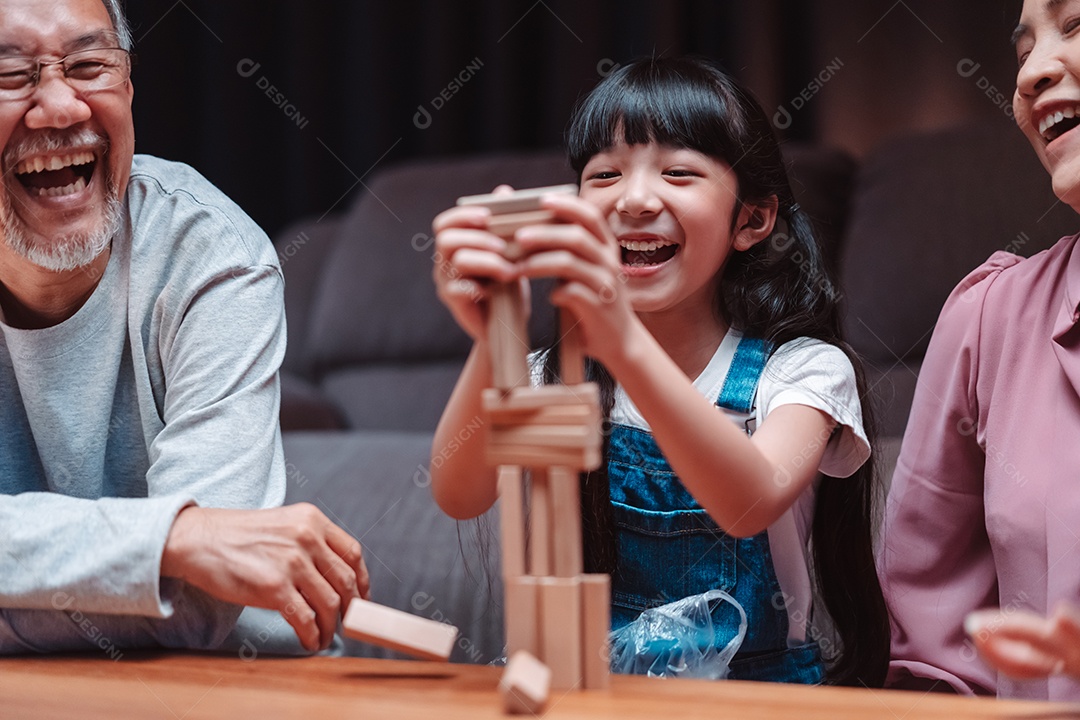 A família feliz asiática da filha joga bloco de madeira de brinquedo em casa.