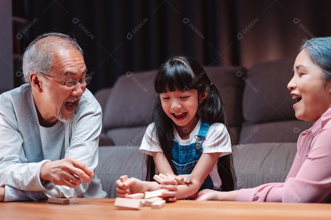 A família feliz asiática da filha joga bloco de madeira de brinquedo em casa.