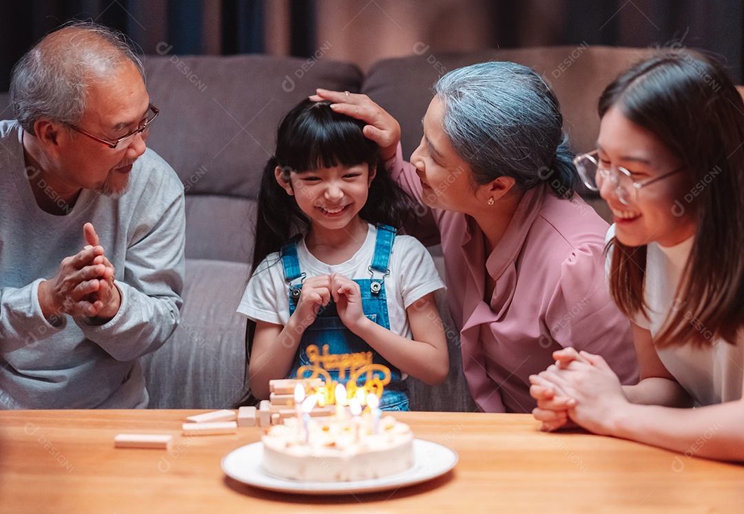 Família feliz asiática de garotinha soprando velas no bolo.
