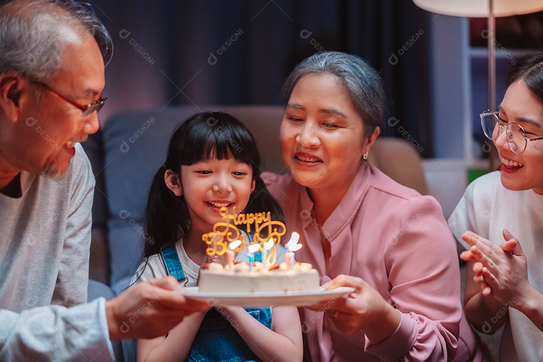 Família feliz asiática de garotinha soprando velas no bolo.