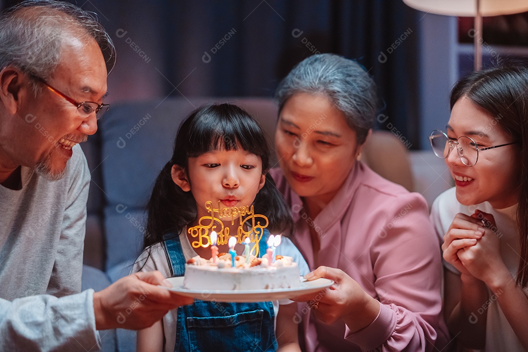 Família feliz asiática de garotinha soprando velas no bolo.