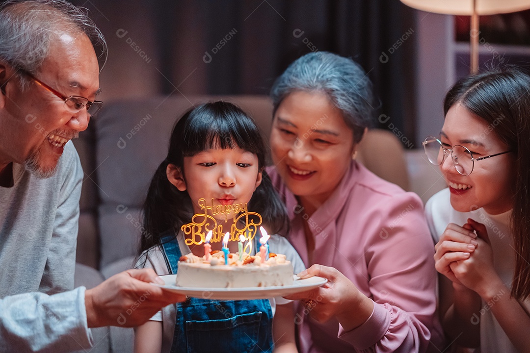 Família feliz asiática de garotinha soprando velas no bolo.