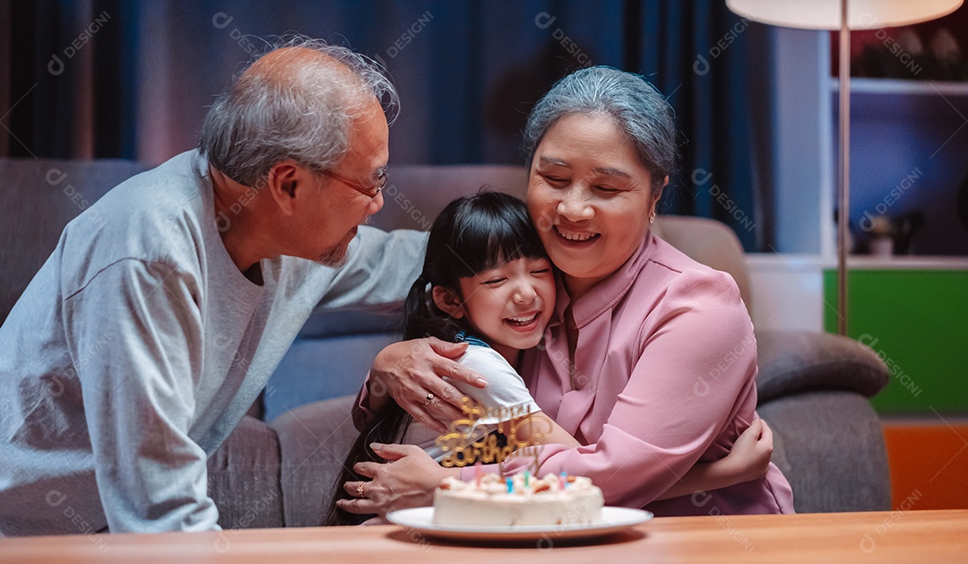 Família feliz asiática de garotinha soprando velas no bolo.