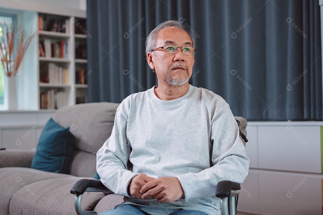 Idoso maduro asiático sente dor de cabeça por estresse sentado em cadeira de rodas na sala de estar.