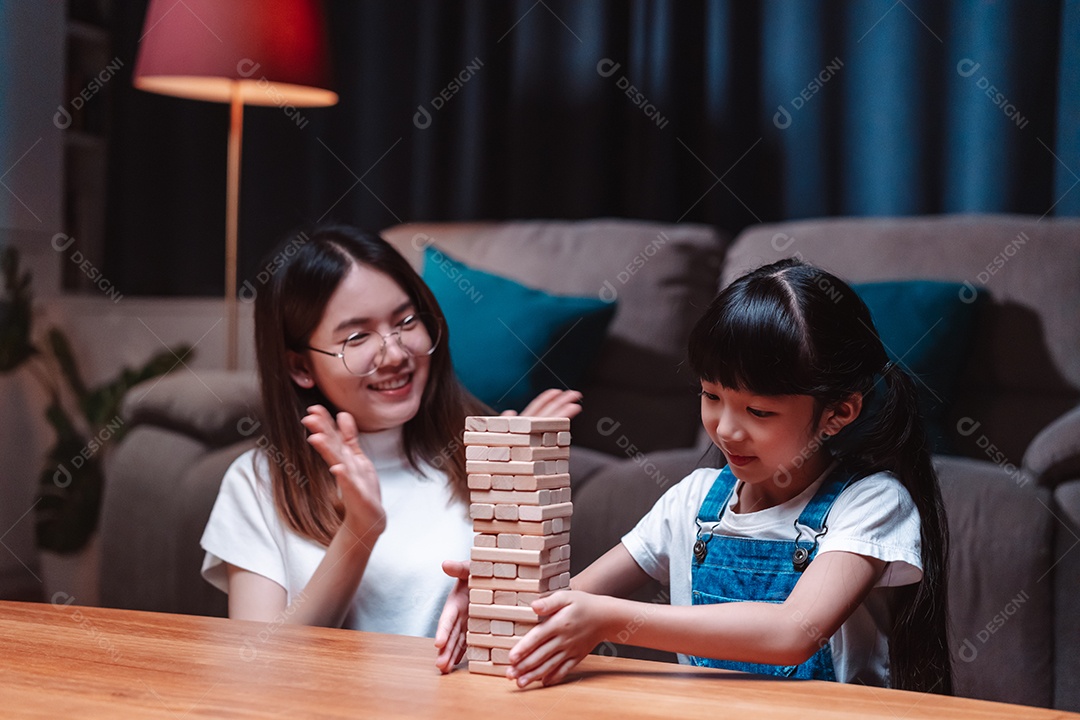 A família feliz asiática da filha joga bloco de madeira de brinquedo em casa.