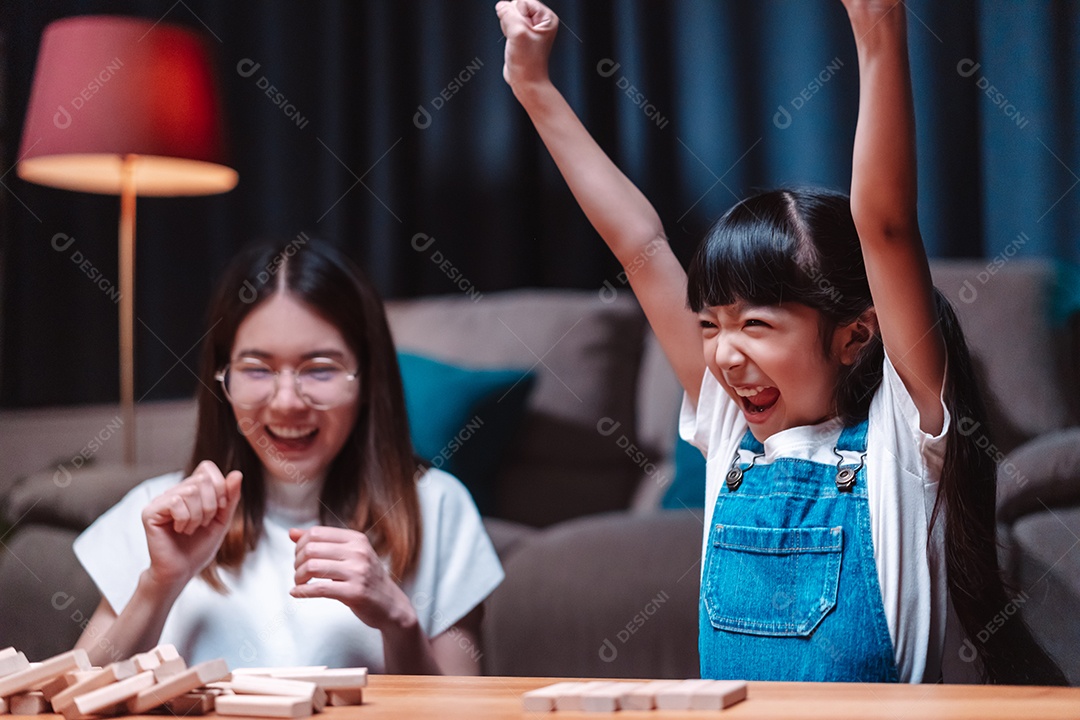 A família feliz asiática da filha joga bloco de madeira de brinquedo em casa.