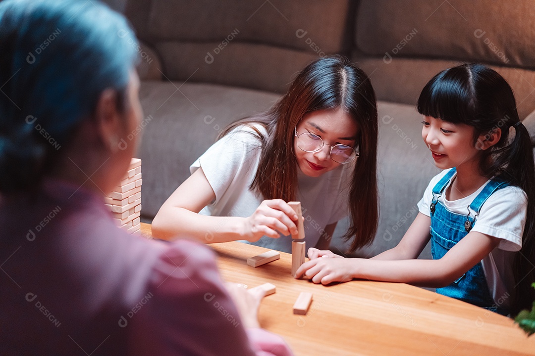 A família feliz asiática da filha joga bloco de madeira de brinquedo em casa.