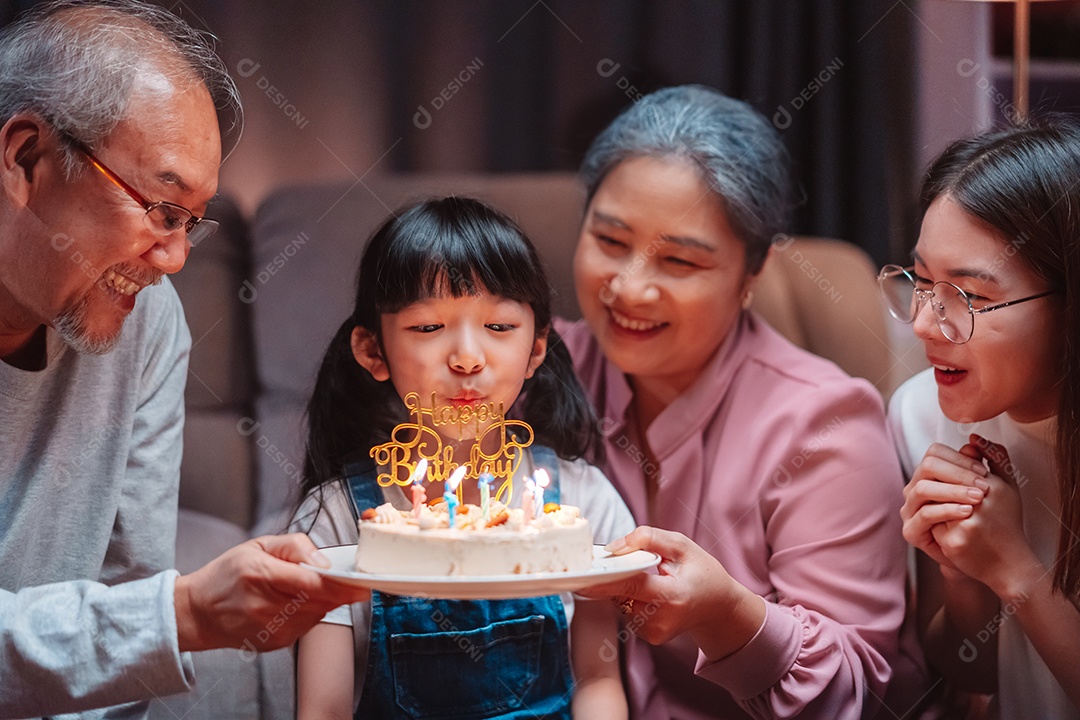 Família feliz asiática de garotinha soprando velas no bolo.