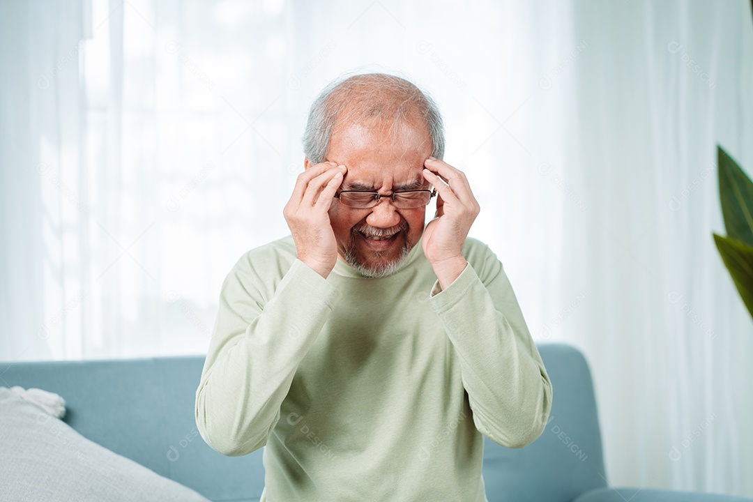 Velho idoso asiático sente dores de cabeça e enxaqueca na sala de estar em casa.