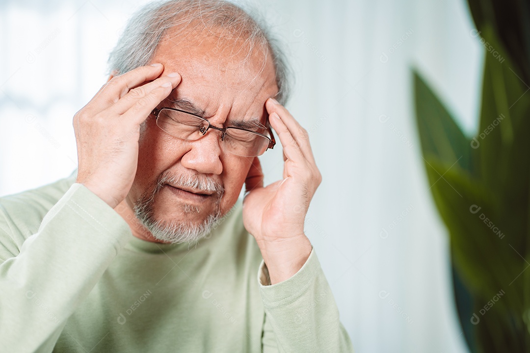 Velho idoso asiático sente dores de cabeça e enxaqueca na sala de estar em casa.
