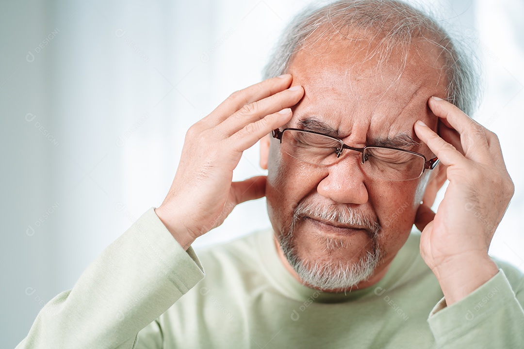 Velho idoso asiático sente dores de cabeça e enxaqueca na sala de estar em casa.