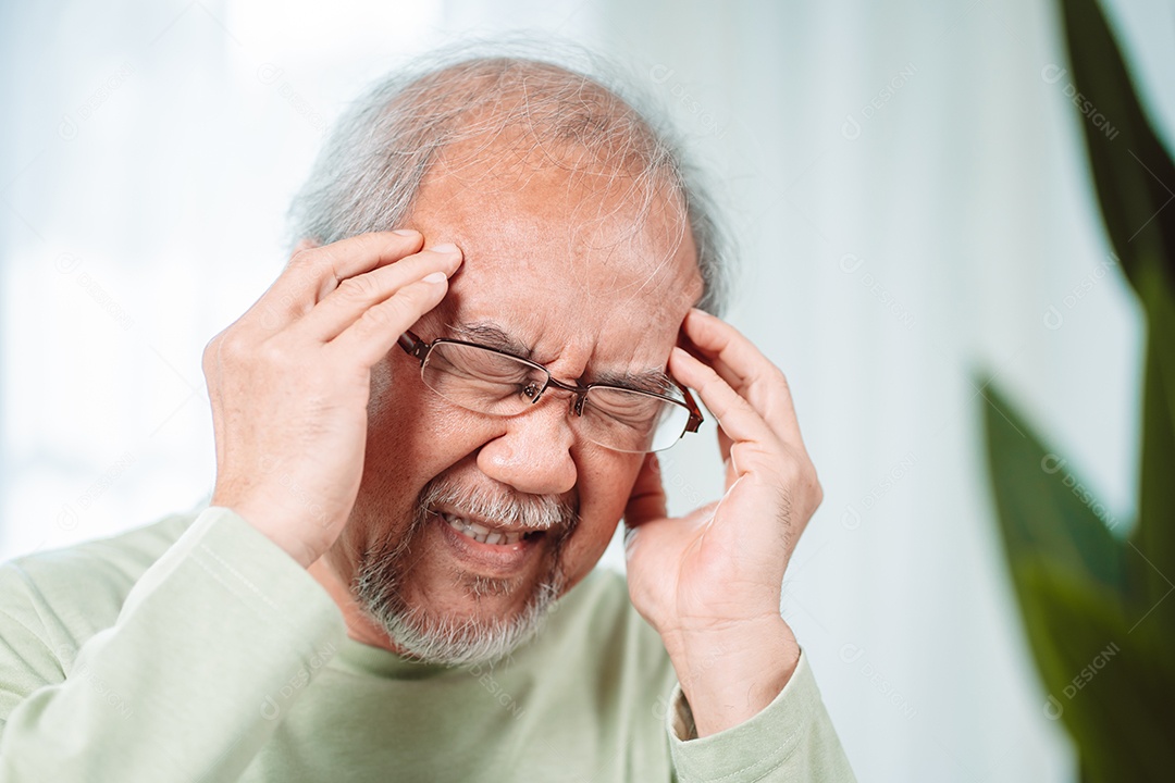 Idoso asiático sente dores de cabeça e enxaqueca na sala de estar em casa.