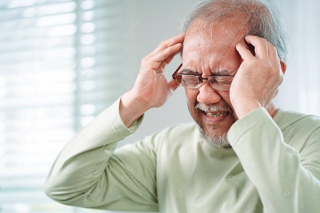 Idoso asiático sente dores de cabeça e enxaqueca na sala de estar em casa.