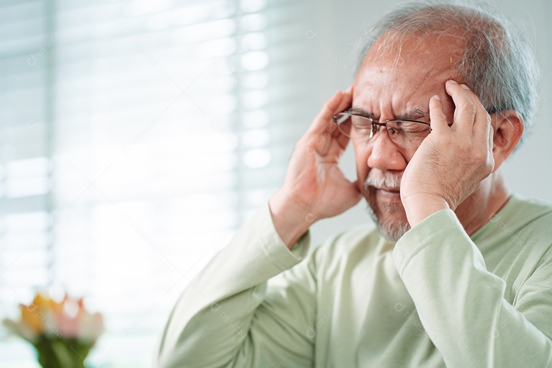 Idoso asiático sente dores de cabeça e enxaqueca na sala de estar em casa.