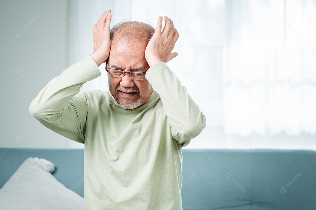 Idoso asiático sente dores de cabeça e enxaqueca na sala de estar em casa.