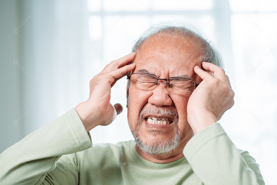Idoso asiático sente dores de cabeça e enxaqueca na sala de estar em casa.