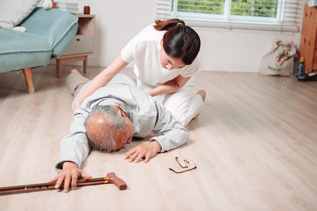 Mulher asiática ajudando o homem sênior que caiu no chão na sala de estar em casa.
