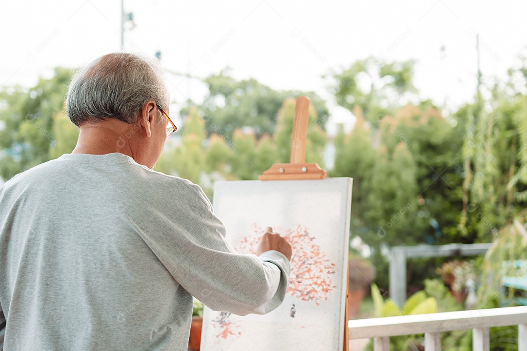 Homem sênior alegre pintando tela no quintal de casa