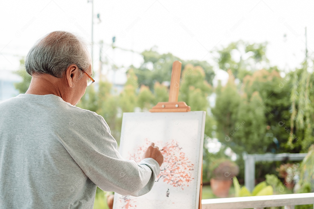 Homem sênior alegre pintando tela no quintal de casa