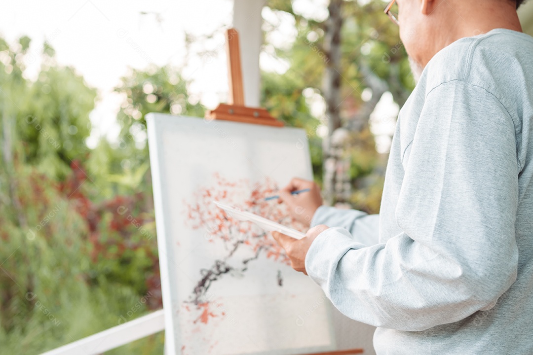Homem sênior alegre pintando tela no quintal de casa