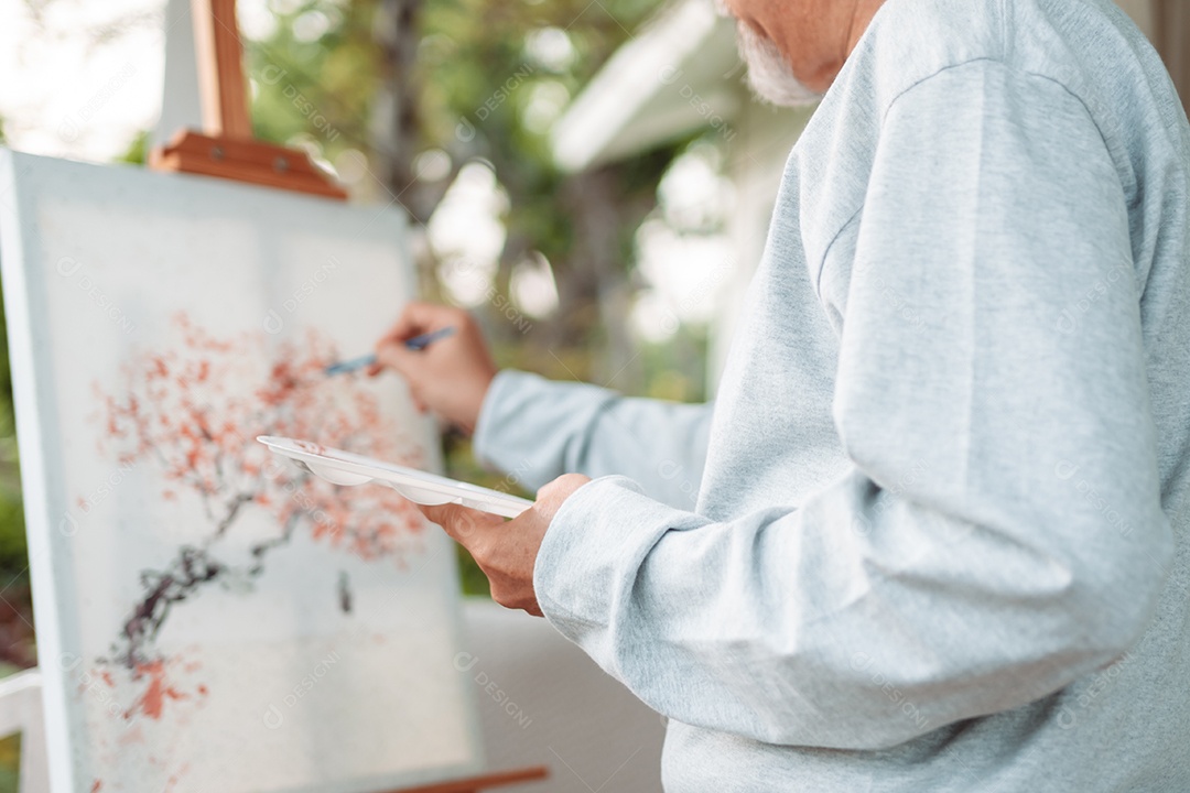 Homem sênior alegre pintando tela no quintal de casa