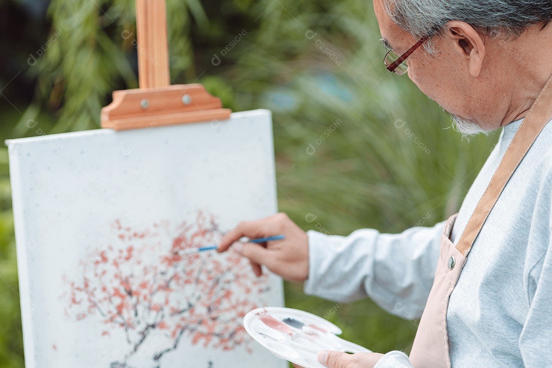 Homem sênior alegre pintando tela no quintal de casa