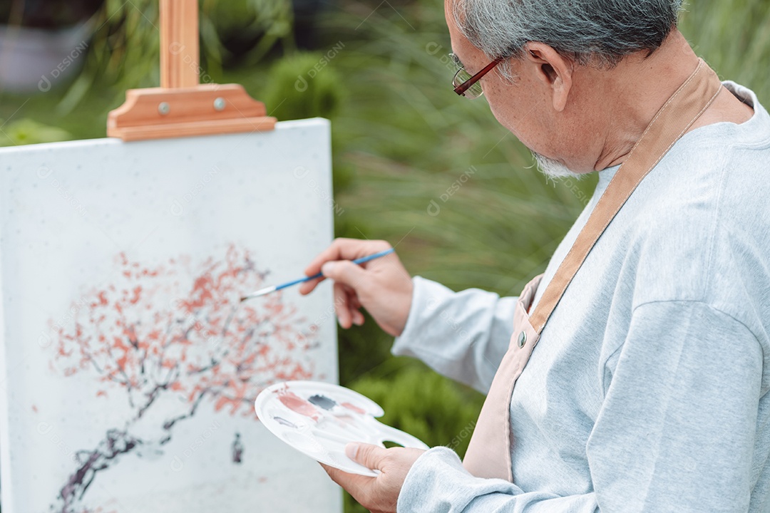 Homem sênior alegre pintando tela no quintal de casa