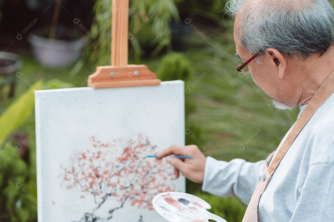Homem sênior alegre pintando tela no quintal de casa