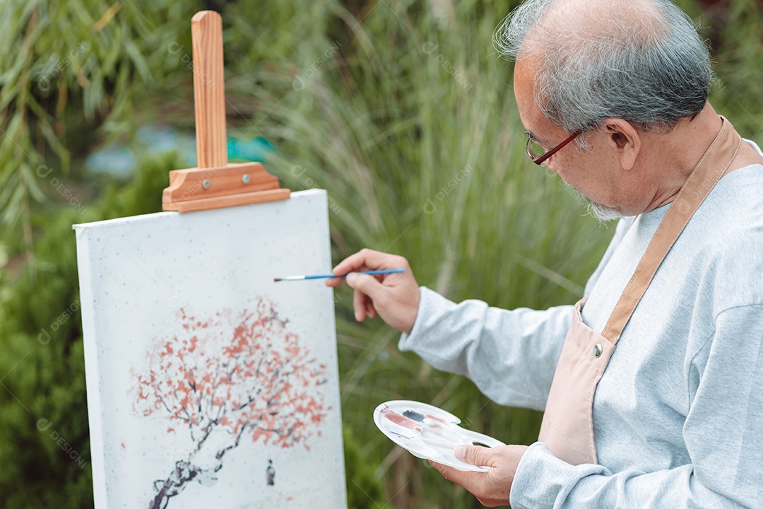 Homem sênior alegre pintando tela no quintal de casa