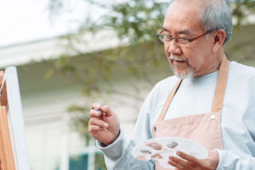 Homem sênior alegre pintando tela no quintal de casa