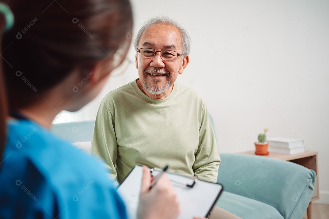 Cuidador asiático falando sobre check-up de paciente masculino sênior na sala de estar em casa.